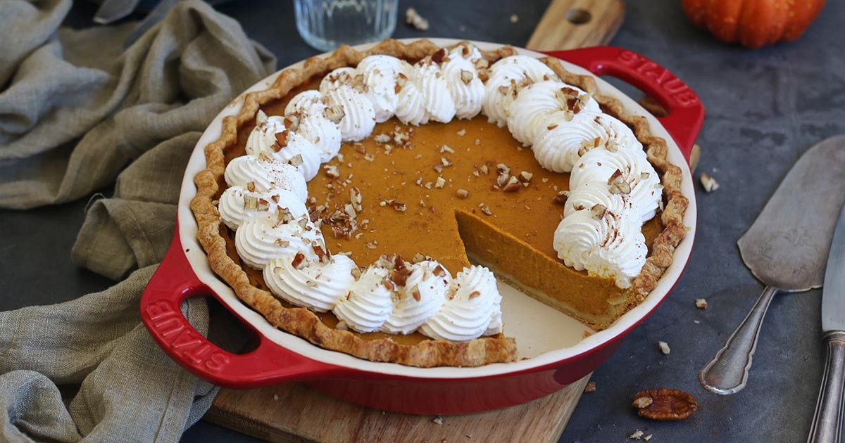 A perfectly baked pumpkin pie with a golden crust and swirls of whipped cream on top, sitting on a rustic wooden table.