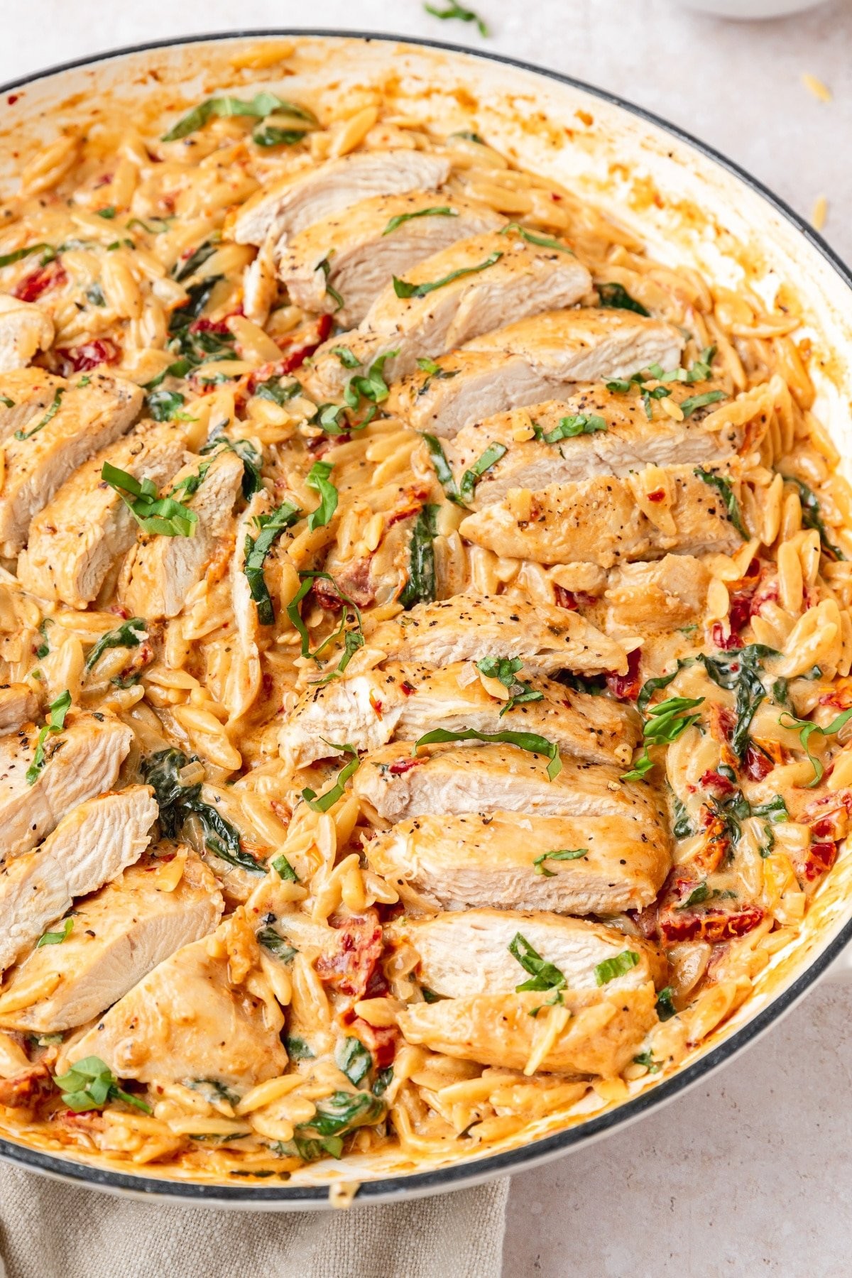A vibrant bowl of creamy Tuscan chicken orzo pasta, garnished with fresh basil, on a rustic wooden table with sun-drenched lighting