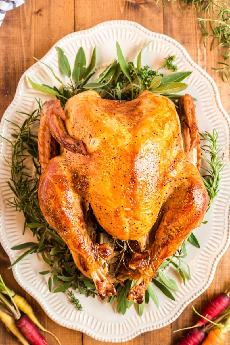 whole golden brown herb roasted turkey with crispy skin on a platter, festive setting with garnish