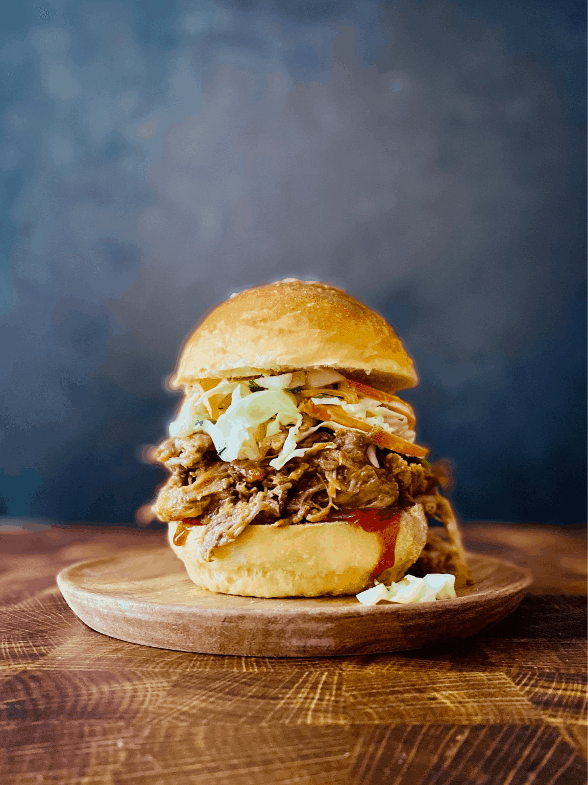 A close-up shot of shredded pulled pork piled high on a brioche bun with creamy coleslaw and a side of pickles. Warm, inviting lighting.