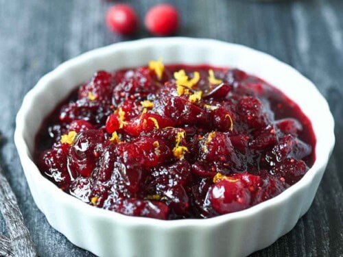Vibrant homemade cranberry sauce with a vanilla bean pod and fresh cranberries in a rustic ceramic bowl, set on a festive holiday table.