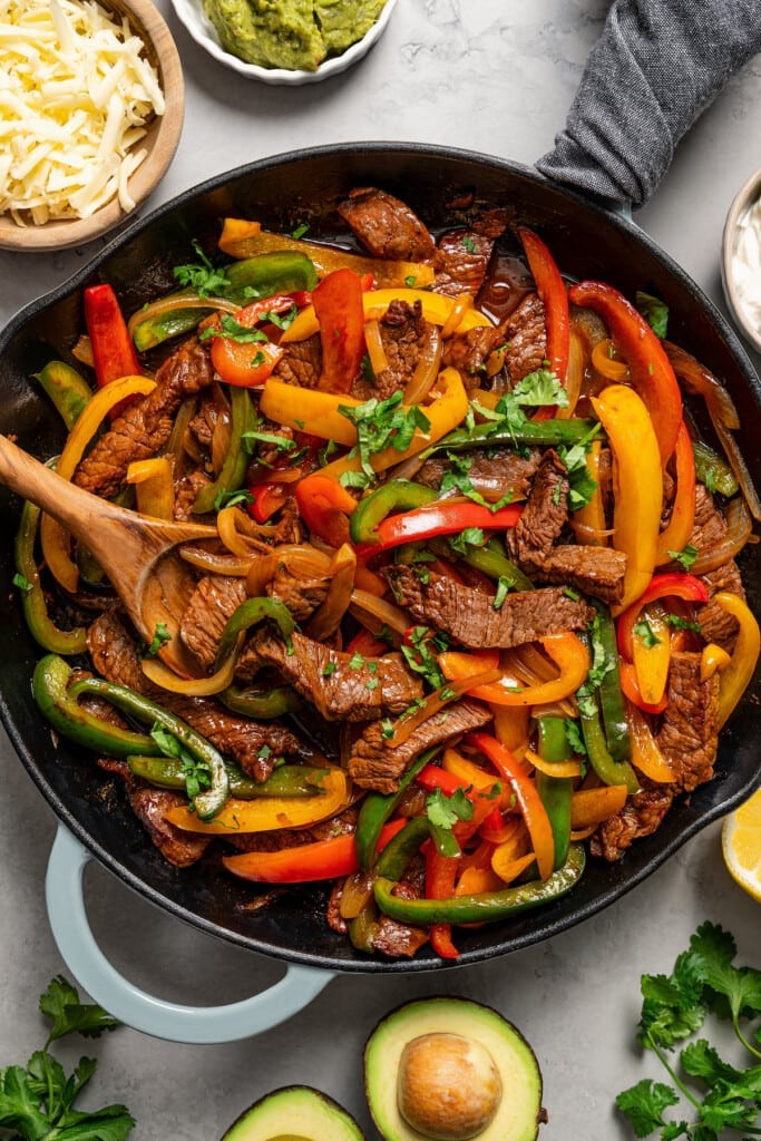 sizzling beef fajitas with bell peppers and onions in a cast iron skillet