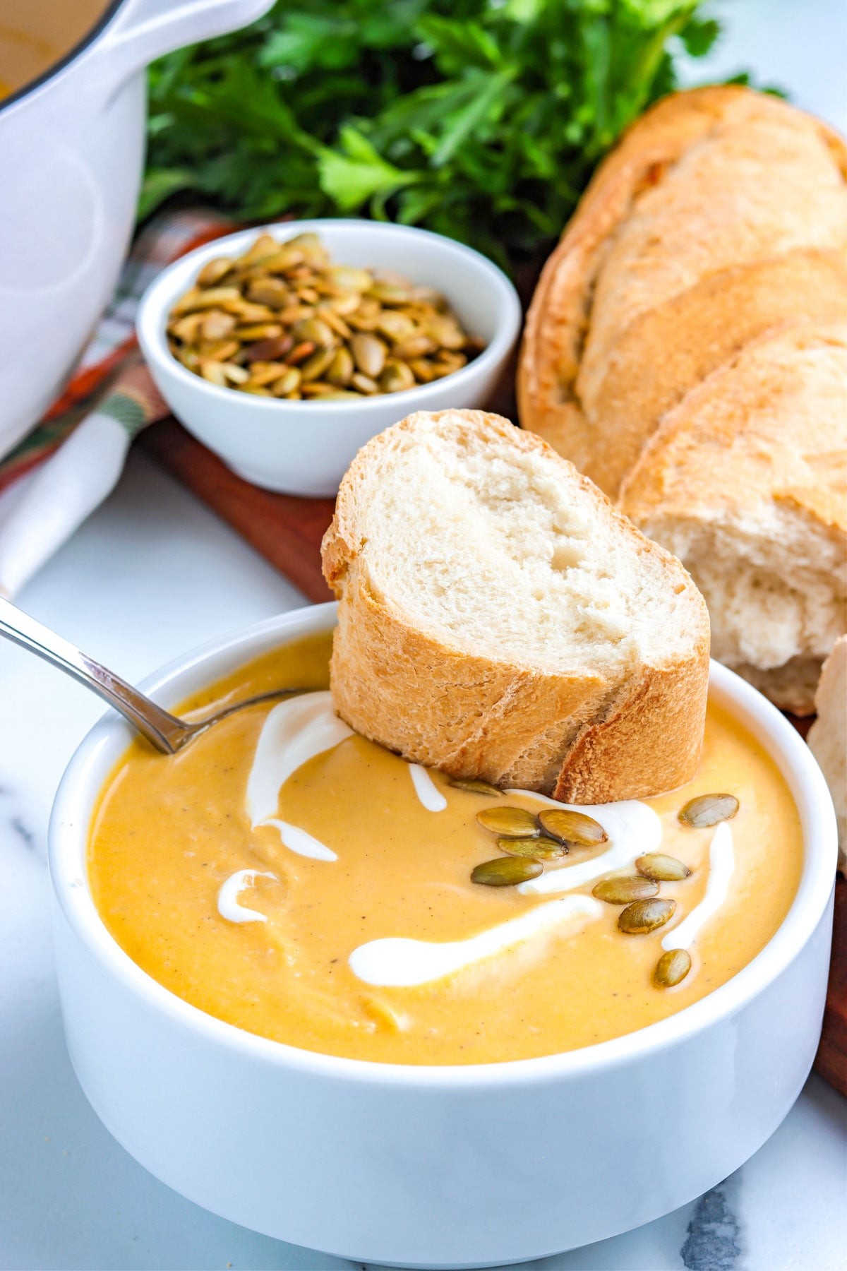 Warm bowl of roasted pumpkin and sage soup with crusty bread, autumn kitchen background