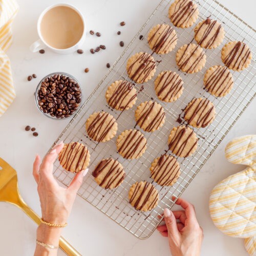 Espresso shortbread cookies arranged artfully on a cooling rack with a steaming cup of coffee in the background