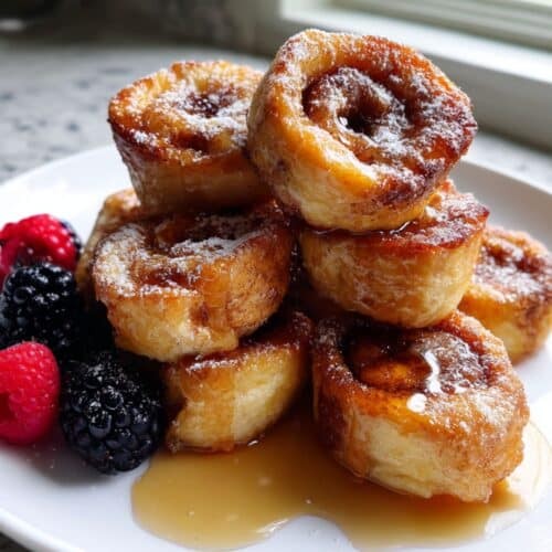 Platter of golden brown cinnamon roll French toast bites drizzled with thick white glaze