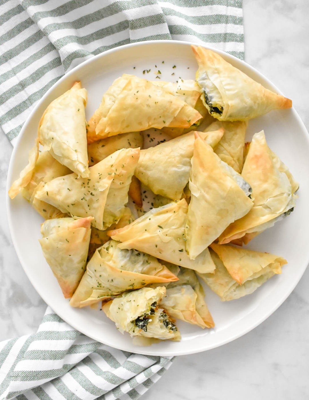 golden brown spinach feta phyllo triangles on a rustic wooden board, garnished with fresh dill