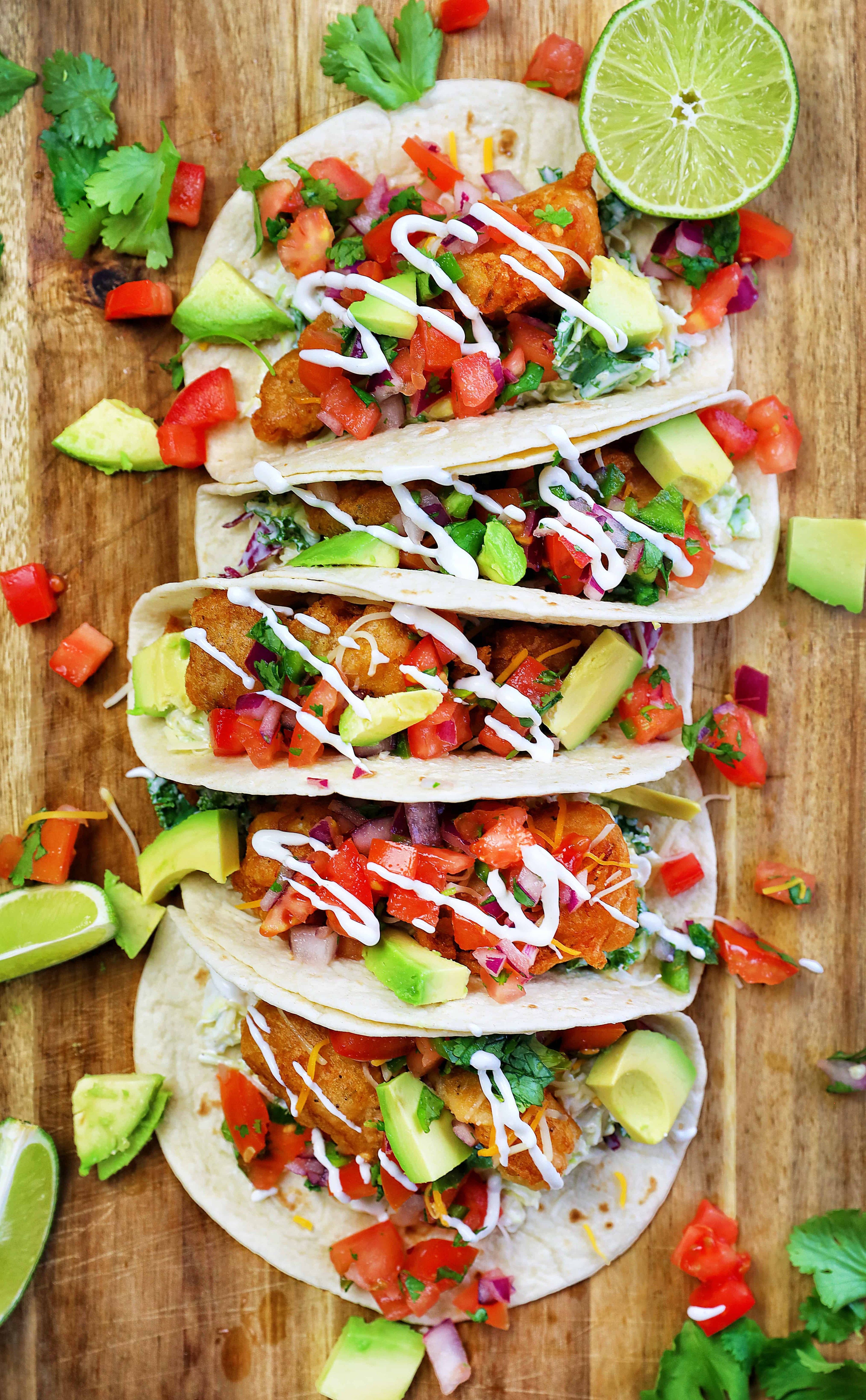 fish taco burrito with Baja sauce on a wooden cutting board, surrounded by lime wedges and cilantro