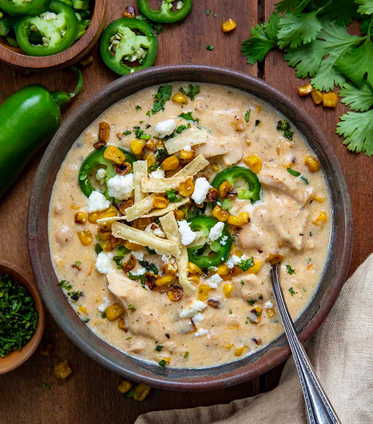 A warm bowl of white chicken chili with roasted corn, garnished with cilantro, on a wooden table, cozy setting.