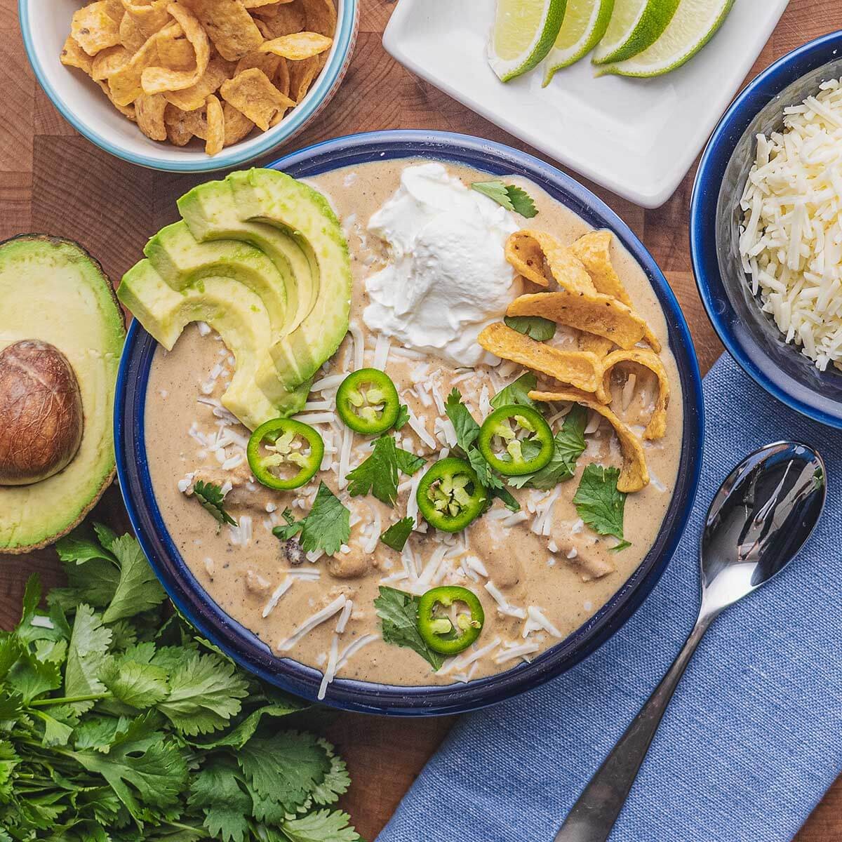 overhead shot of a steaming bowl of white chicken chili with fresh toppings like avocado, cilantro, and sour cream, on a rustic wooden table