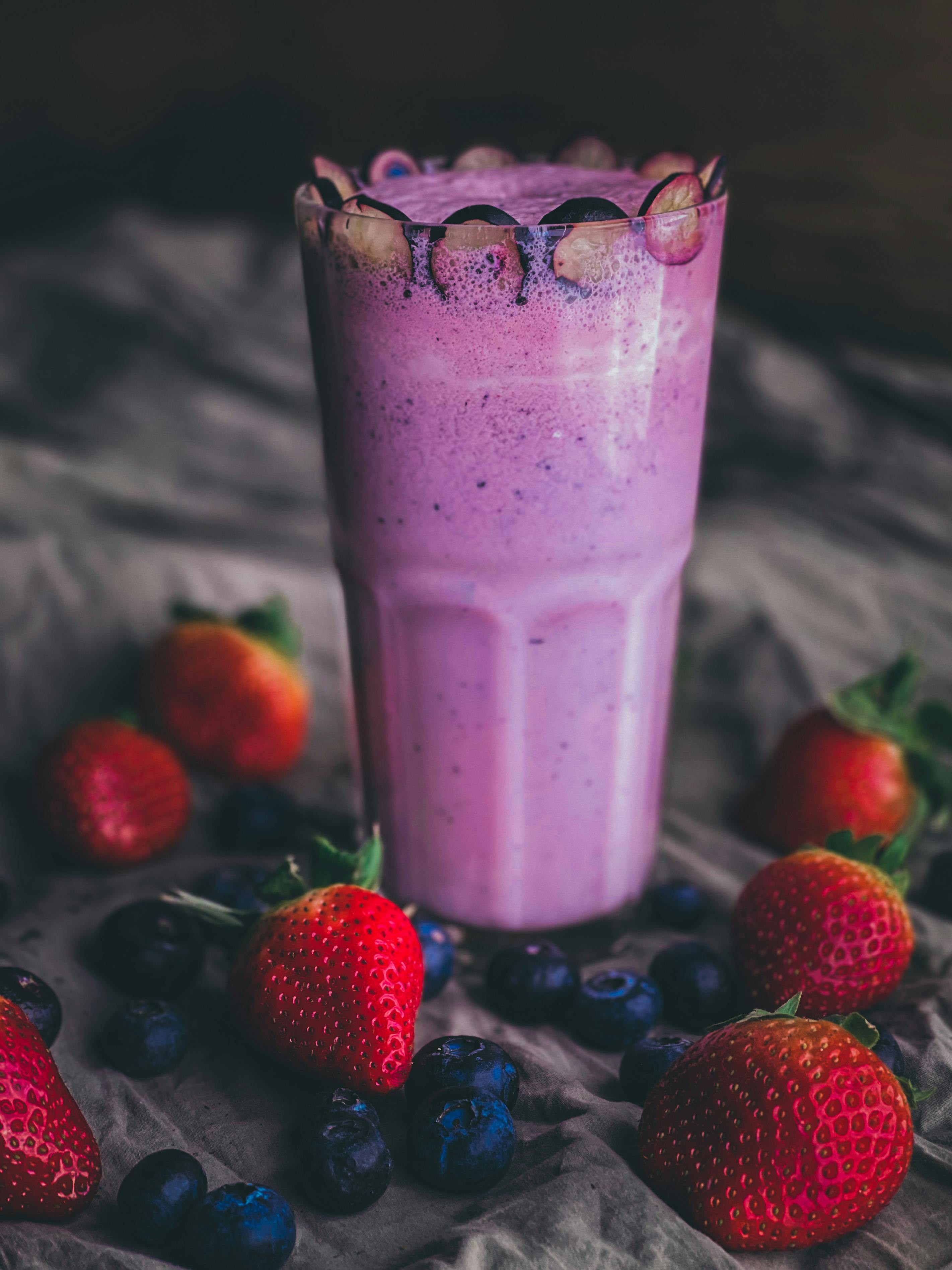 close up shot of a vibrant berry smoothie in a glass with berries and a spice shaker nearby