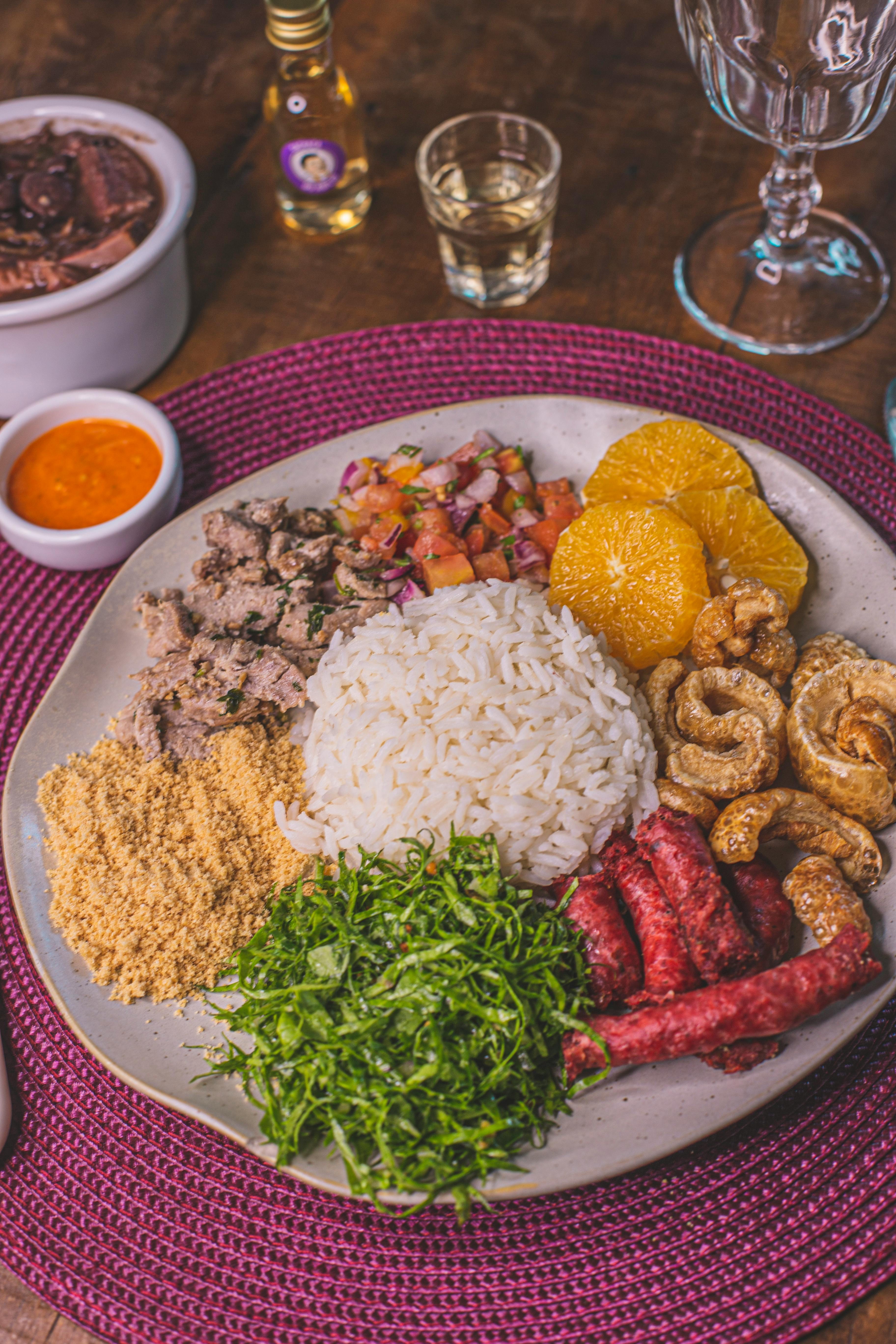 A rustic table set with a steaming bowl of feijoada and a separate plate of sarapatel, garnished with fresh herbs