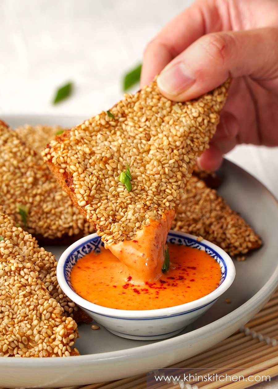 Golden brown crispy sesame shrimp toast triangles with dipping sauce on a white plate