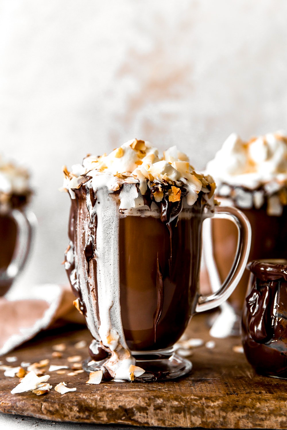 A steaming mug of coconut hot chocolate topped with tropical whipped cream and toasted coconut flakes, styled for a cozy yet exotic feel.