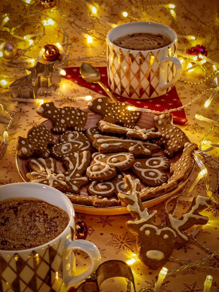 beautifully decorated gingerbread cookies on a festive tray with holiday lights and cinnamon sticks