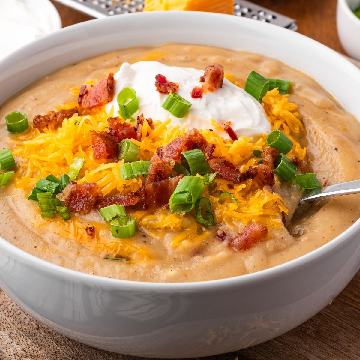 a bowl of loaded baked potato soup with toppings on a wooden table