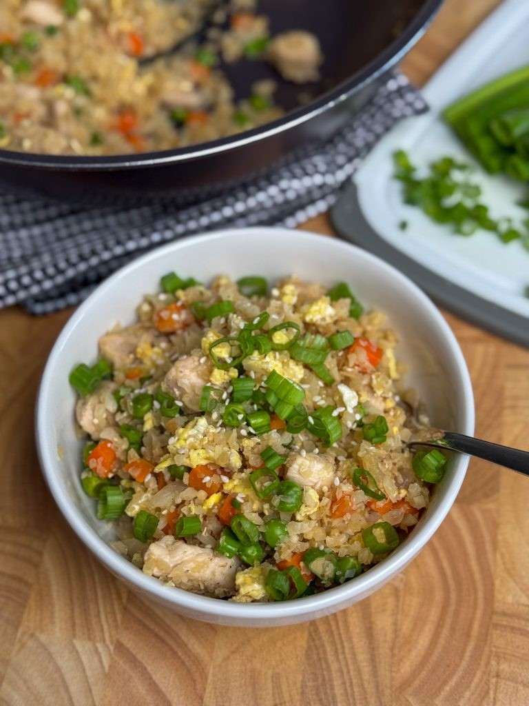 Cauliflower rice chicken stir-fry in a wok, garnished with sesame seeds and green onions