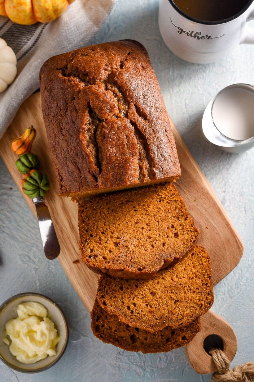 overhead shot of sliced pumpkin bread on a wooden cutting board with a knife and a cup of coffee