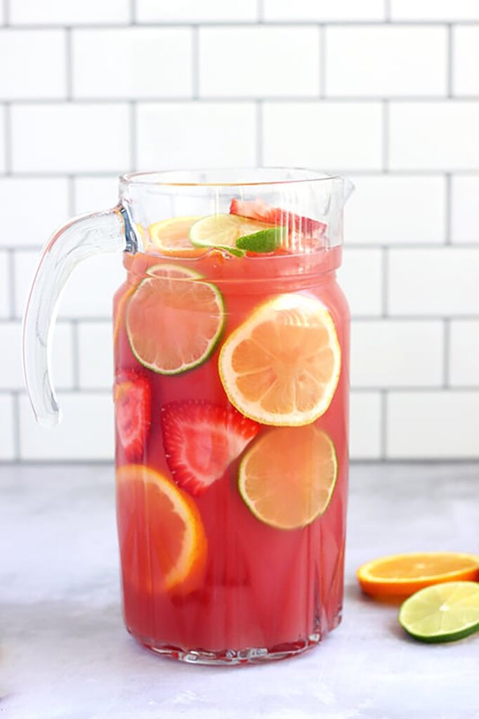 Refreshing fruit punch in a large glass pitcher with ice and fruit slices
