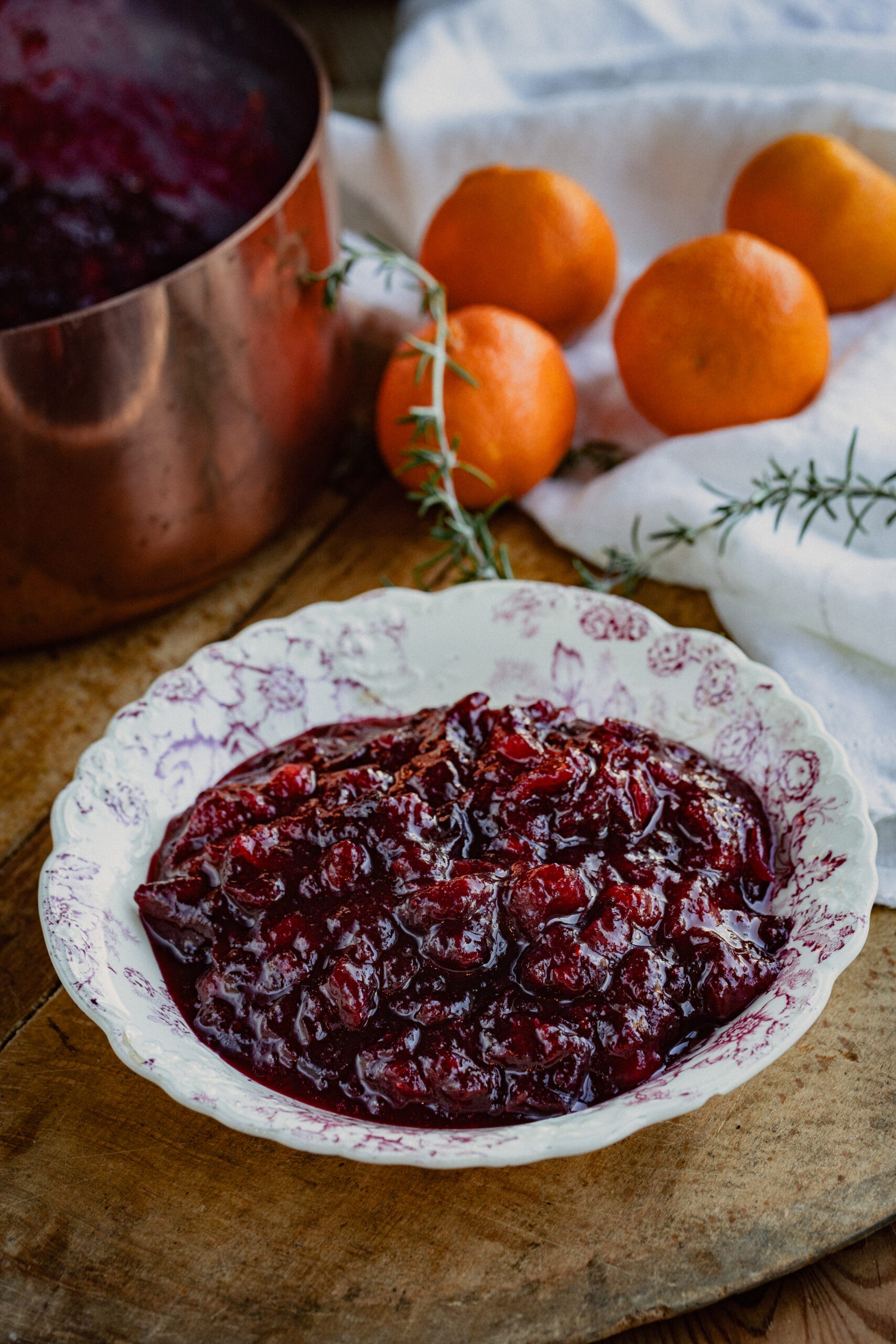 Vibrant homemade cranberry sauce in a rustic ceramic bowl with fresh cranberries and orange zest, on a wooden table, holiday setting