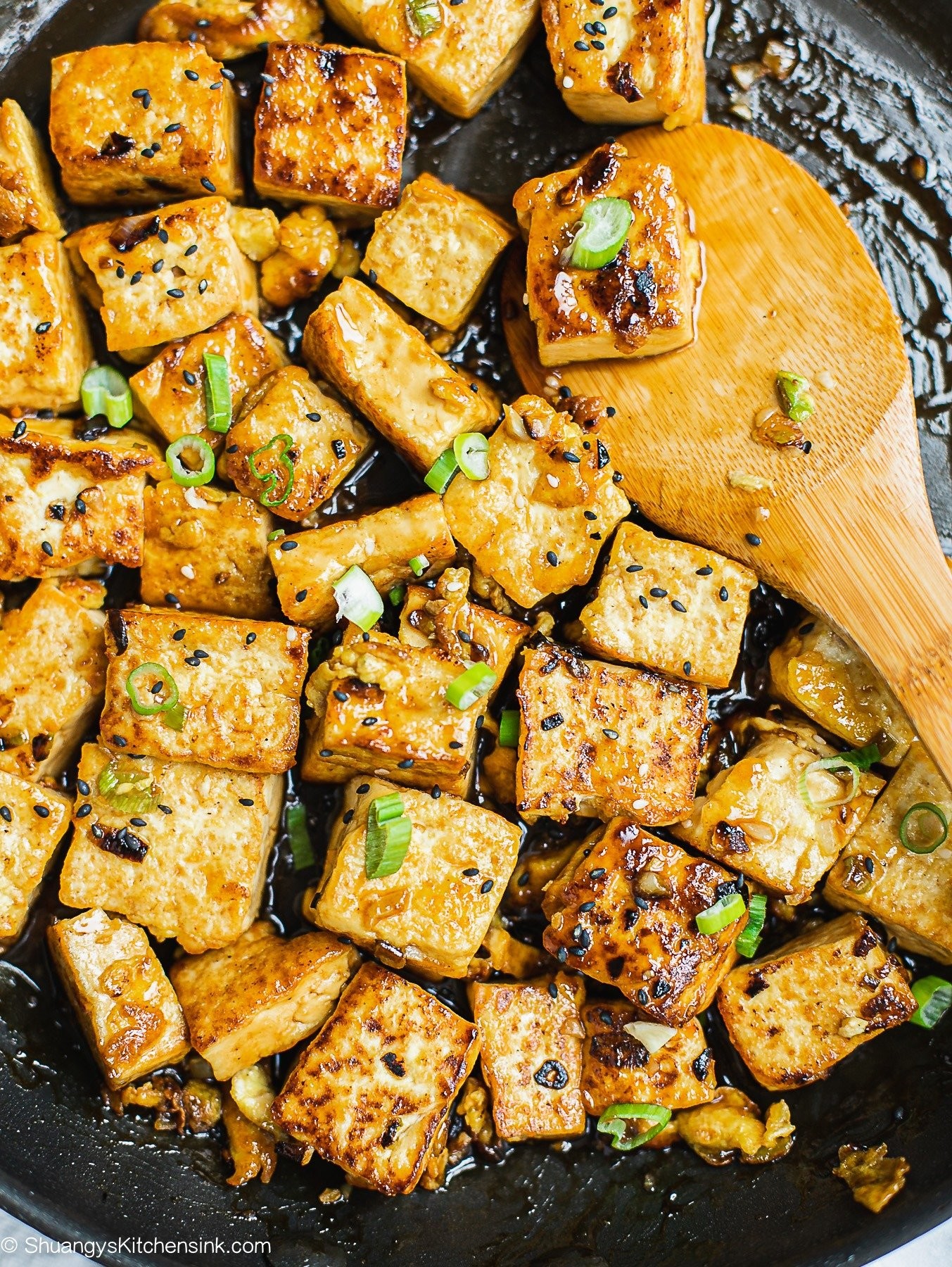 Garlic butter tofu stir-fry in a wok, garnished with sesame seeds and green onions