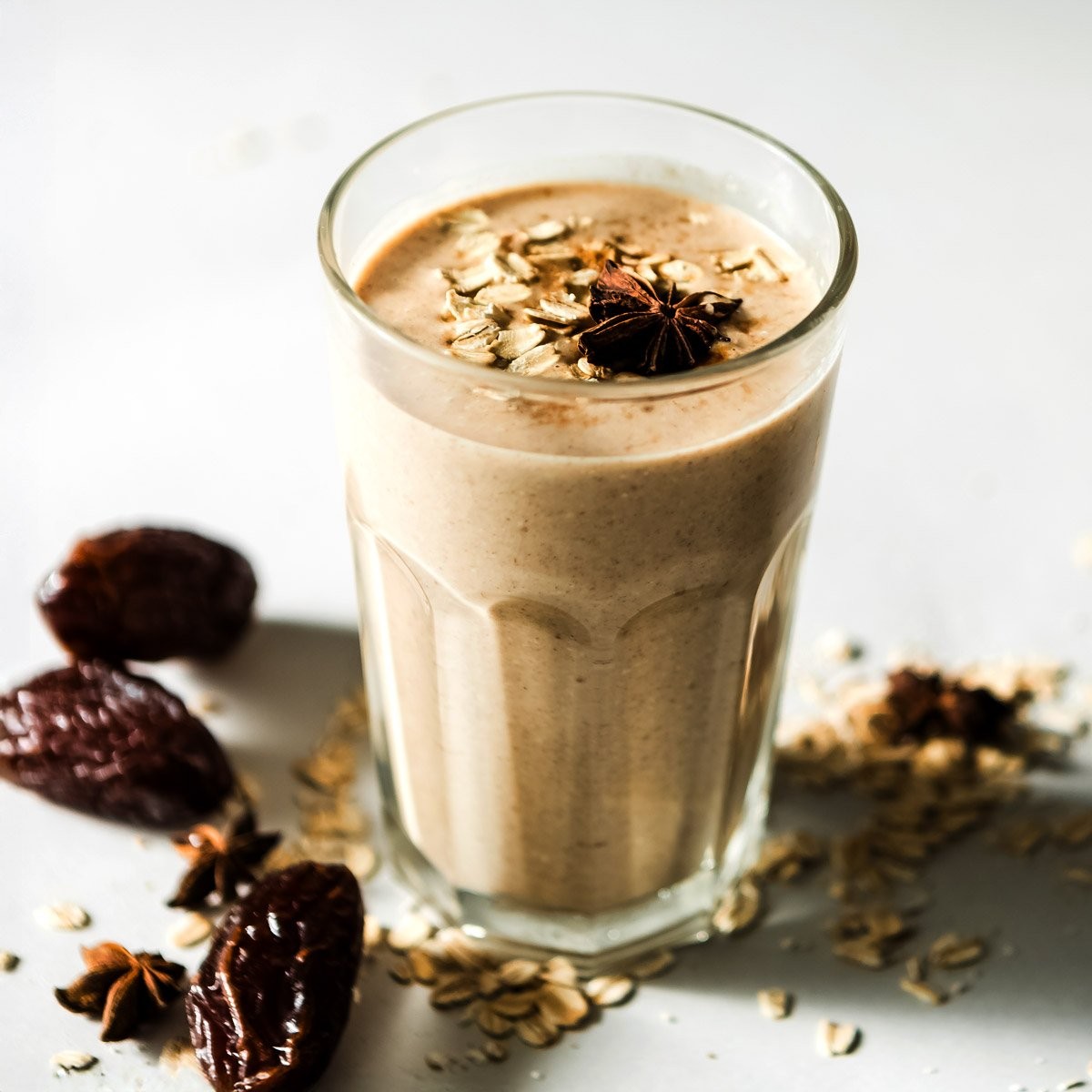 close up of a date and cinnamon smoothie in a glass with dates and cinnamon sticks scattered around
