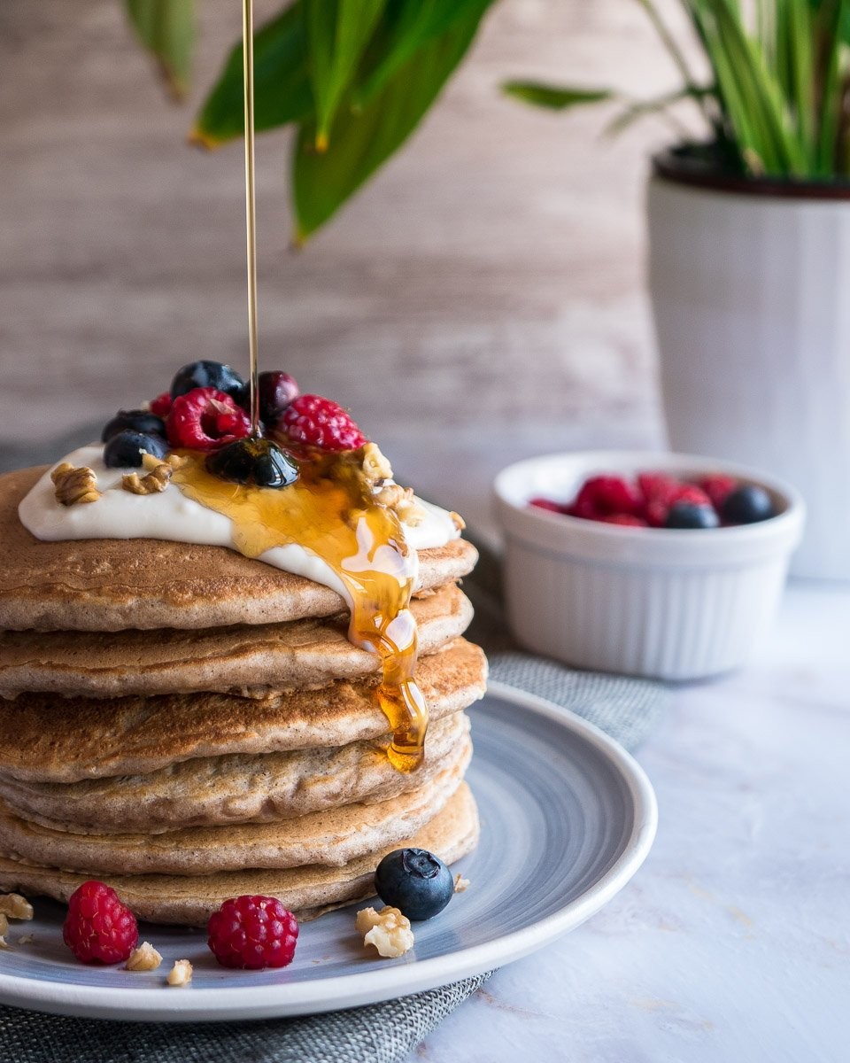 A stack of fluffy pear pancakes with a dusting of powdered sugar and a side of maple syrup, garnished with fresh pear slices and a sprinkle of ginger.