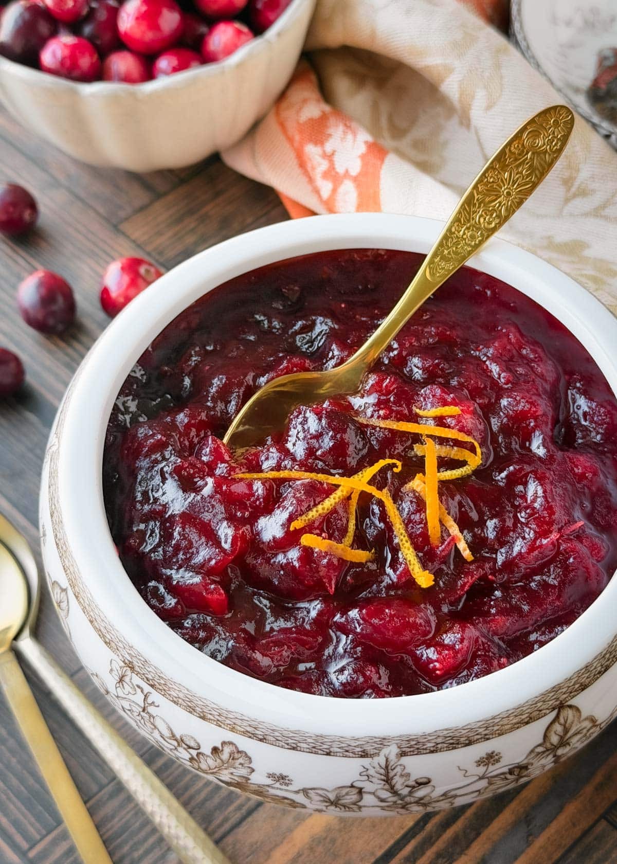 Homemade cranberry sauce in a beautiful glass bowl with a spoon, glistening ruby red with orange zest garnish