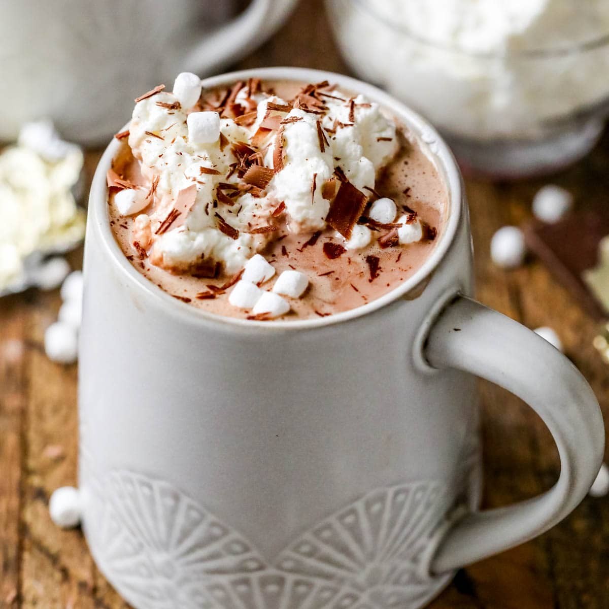 Mug of creamy white chocolate hot cocoa with whipped cream and chocolate shavings on a cozy background