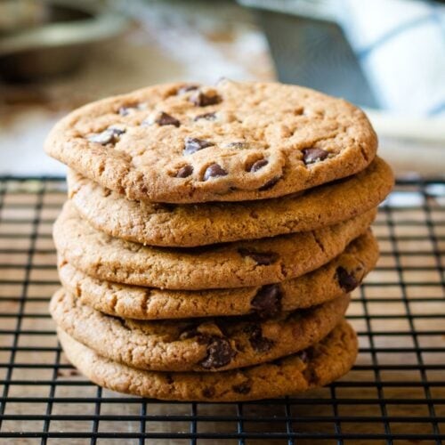 close-up shot of perfectly baked crispy-edged chocolate cookies on a cooling rack, some with melted chocolate chips visible, a hand reaching for one