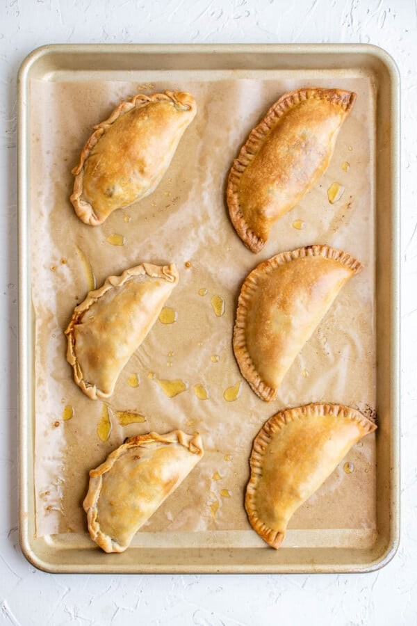 Close-up shot of golden brown beef and cheese empanadas on a baking sheet