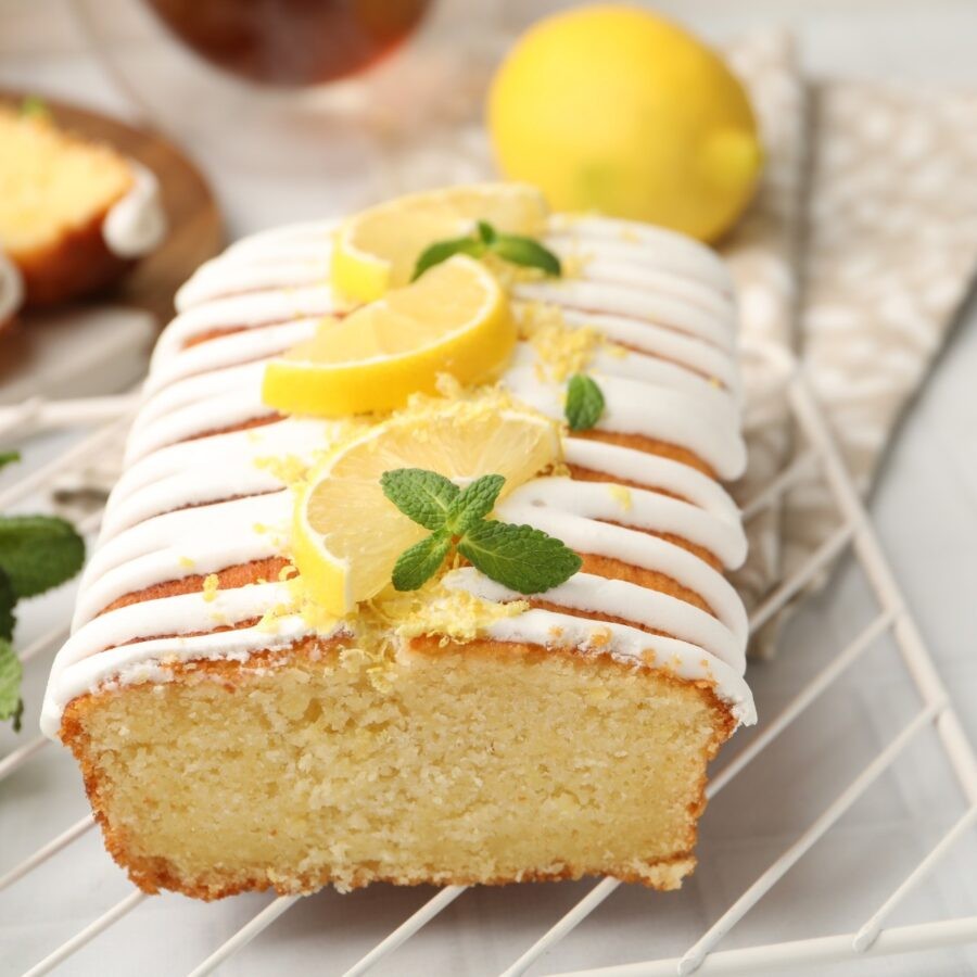 Brightly lit slice of lemon yogurt cake on a white plate with fresh lemon slices and mint, natural light, soft focus