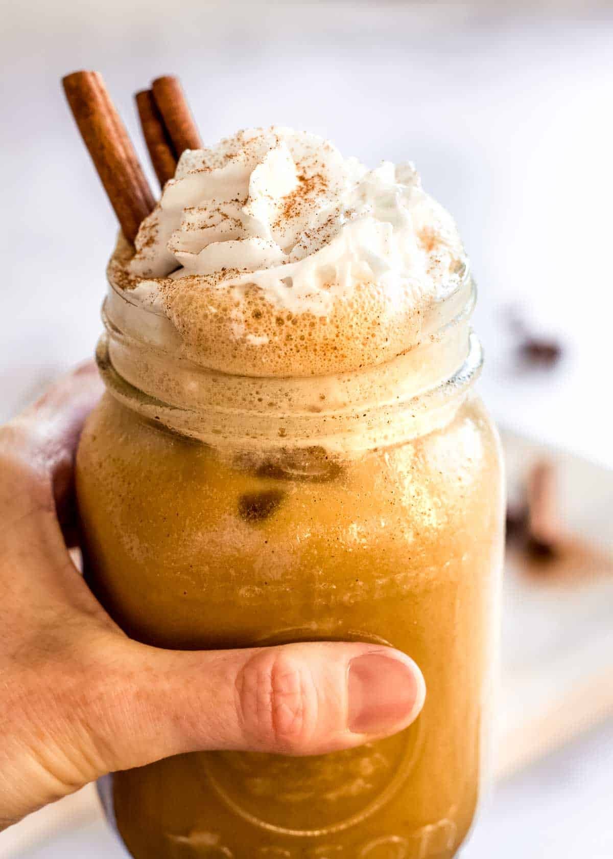 A creamy orange Pumpkin Spice Latte Smoothie in a tall glass with whipped cream and cinnamon on top.