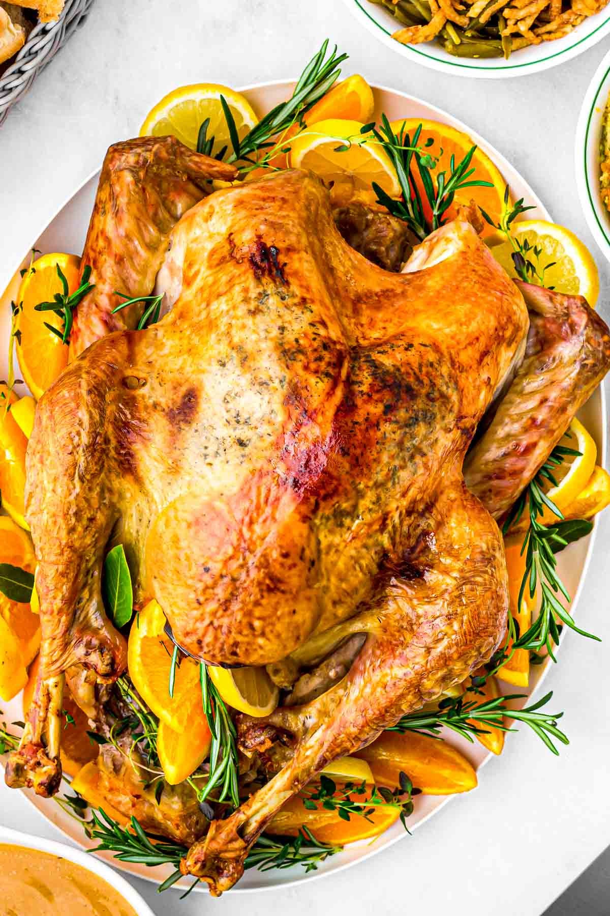 A beautifully golden pan-roasted turkey, glistening with citrus and herbs, on a carving board with fresh rosemary and lemon slices.