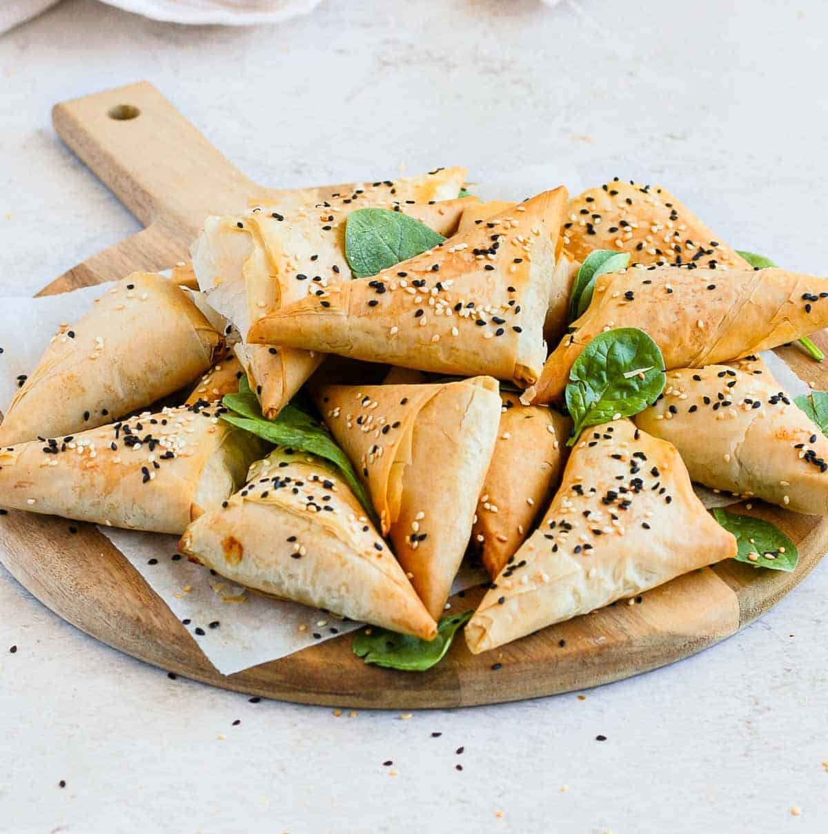 Golden brown spinach feta pastry triangles arranged beautifully on a rustic wooden board, garnished with fresh herbs