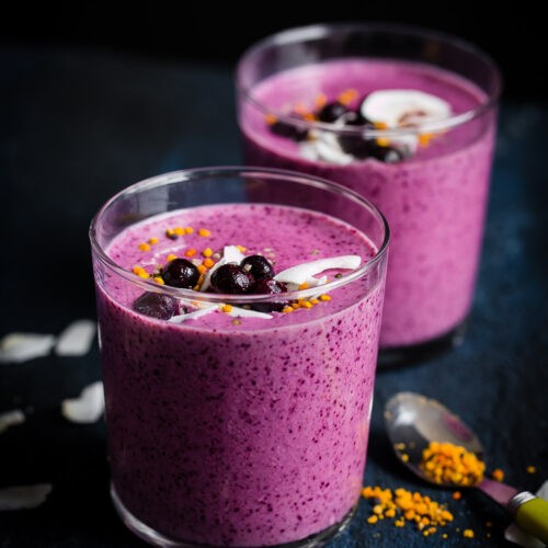 Close-up shot of a vibrant pink Berry Cookie Dough Smoothie in a glass with berries and cookie dough on the side