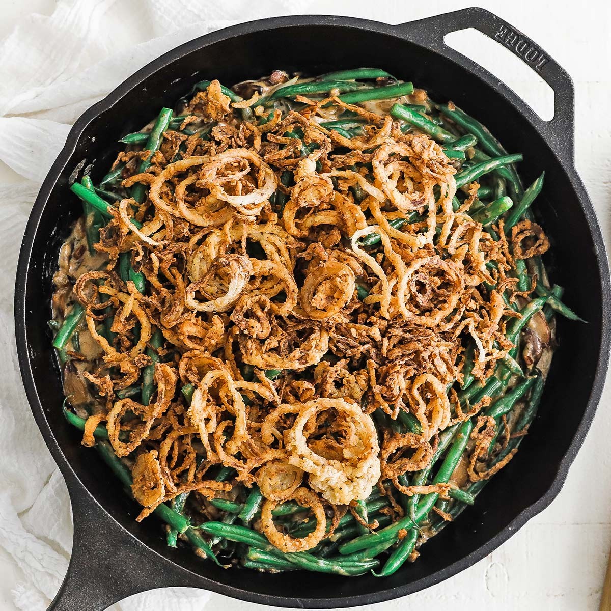 Green bean casserole in a rustic cast iron skillet, garnished with fresh herbs and crispy fried onions, close-up, warm lighting