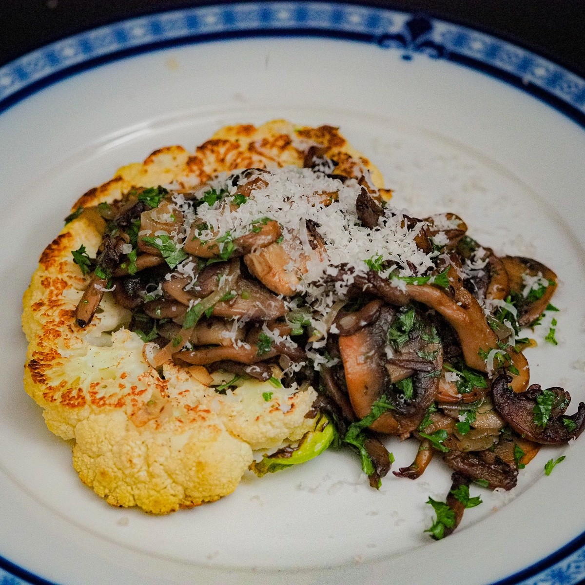 Close-up of perfectly seared cauliflower steaks topped with balsamic glaze and sauteed mushrooms, garnished with fresh herbs