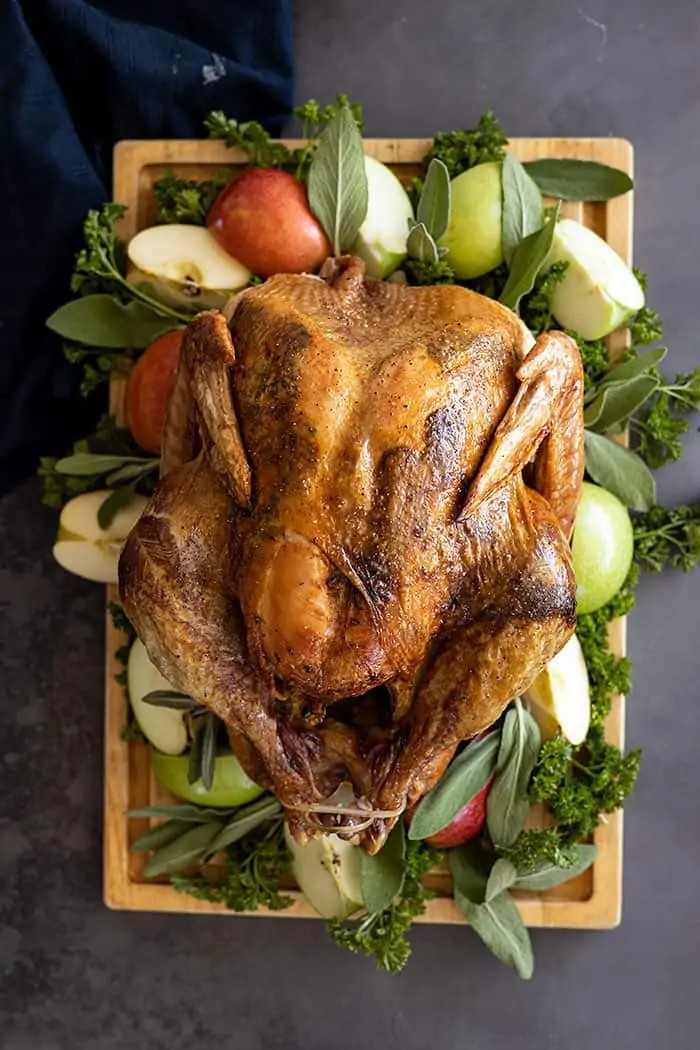 beautifully roasted whole turkey with glossy, crispy peppered skin, garnished with fresh herbs on a wooden cutting board
