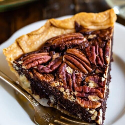 slice of fudgy chocolate pecan pie on a white plate with a fork, garnished with powdered sugar