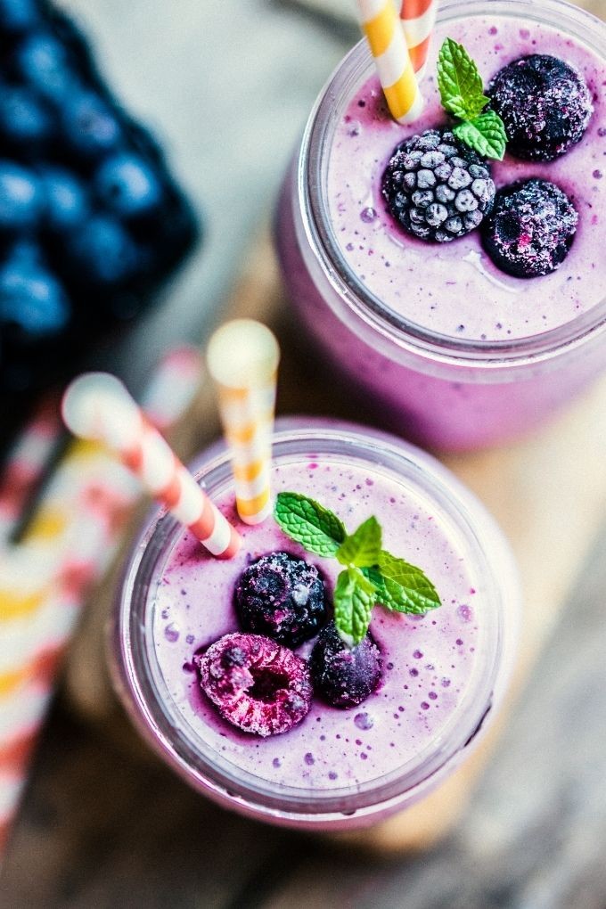 Close-up of a vibrant pink mixed berry protein smoothie in a glass with berries and protein powder scattered around it