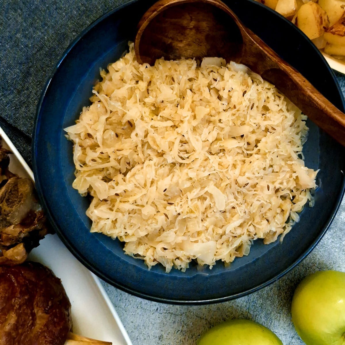 A rustic wooden bowl filled with vibrant sauerkraut and a sweet apple compote, garnished with fresh parsley.