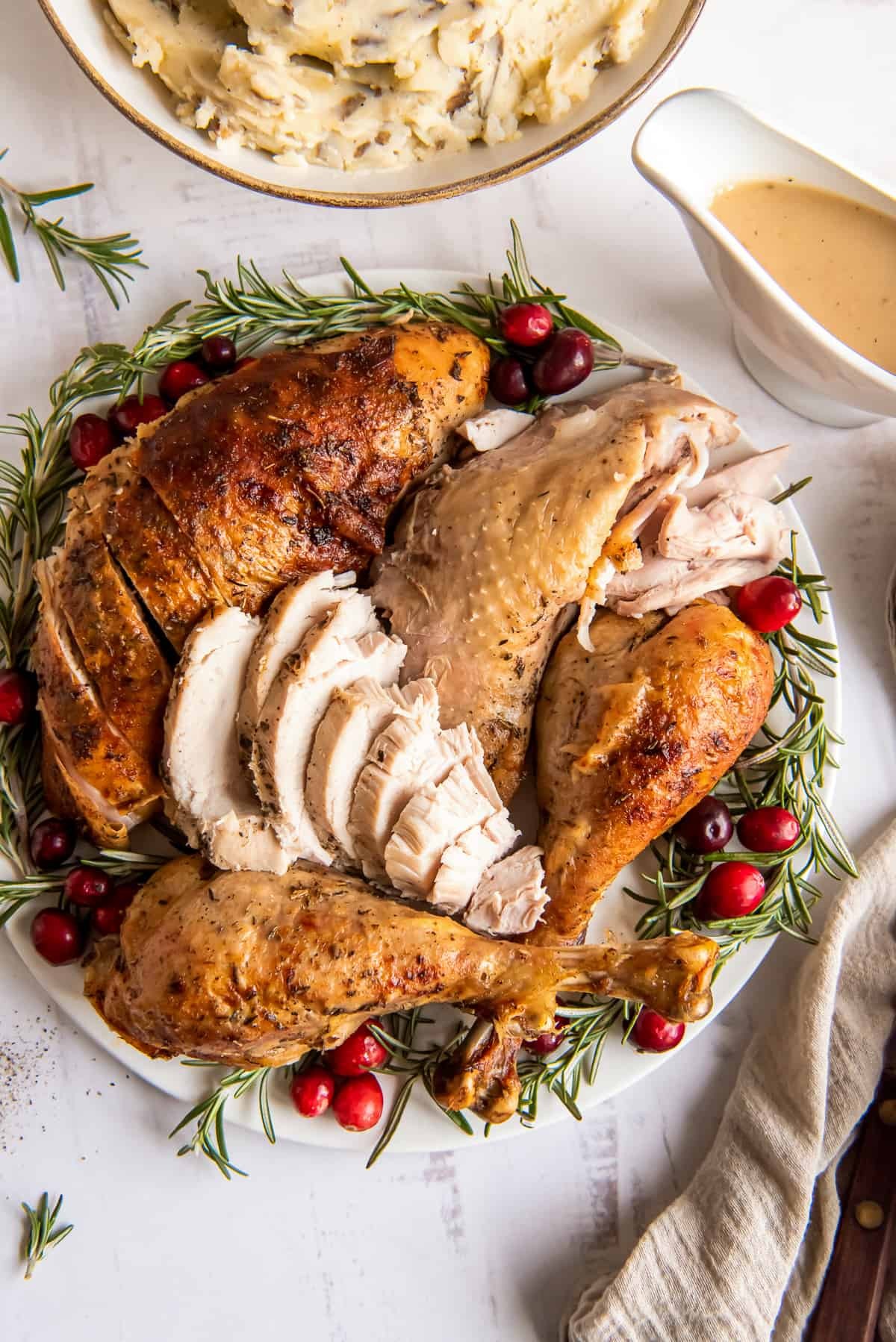beautifully roasted whole turkey on a platter with fresh herbs and cranberries