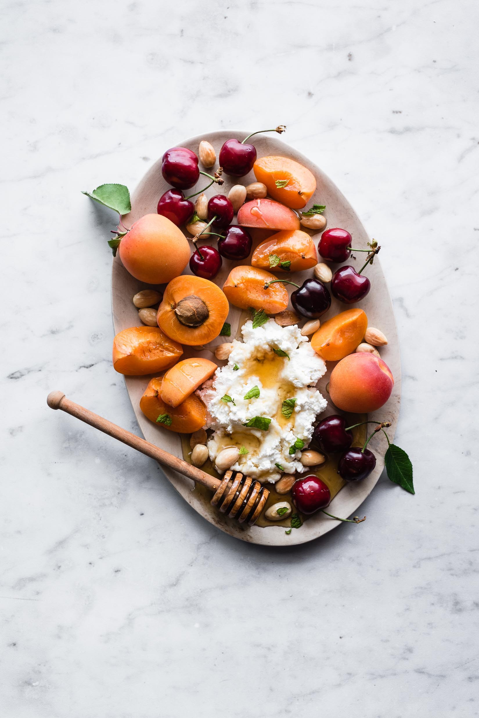 overhead shot of a colorful stone fruit picnic platter with various fruits, cheeses, and nuts