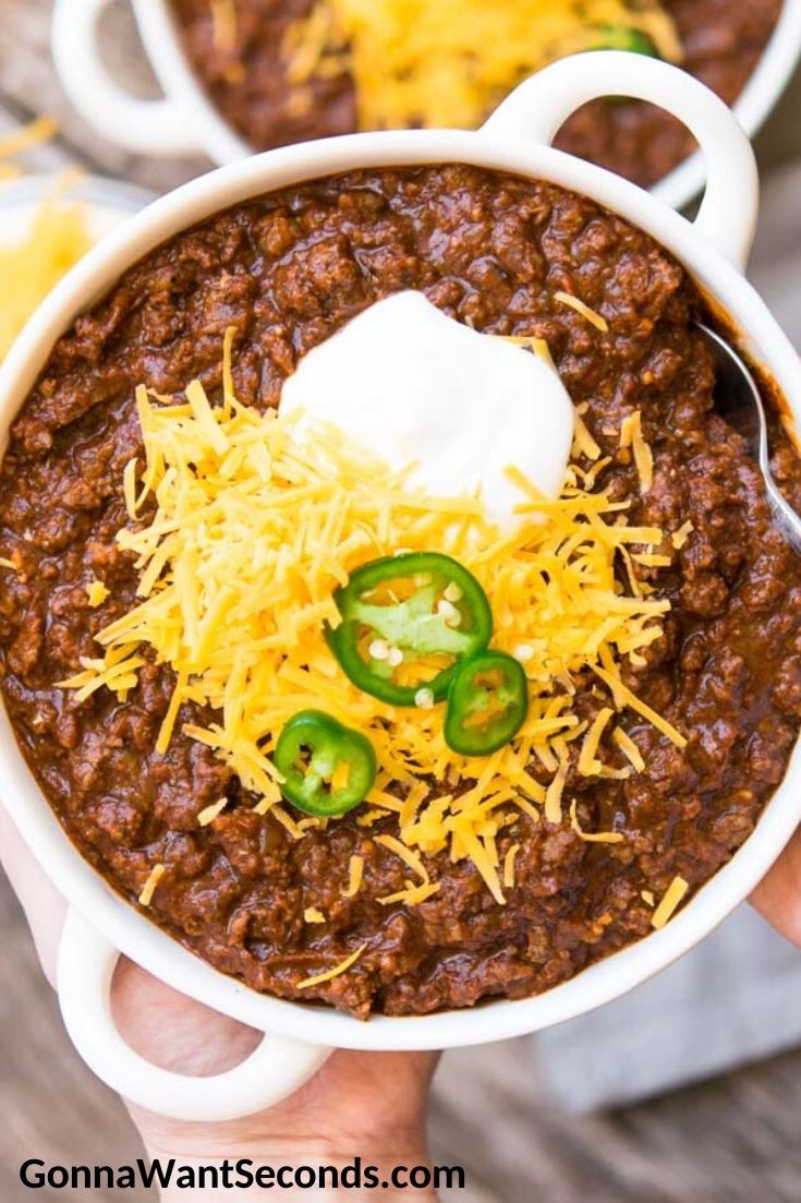 a steaming bowl of beef and bean chili topped with shredded cheese and sour cream