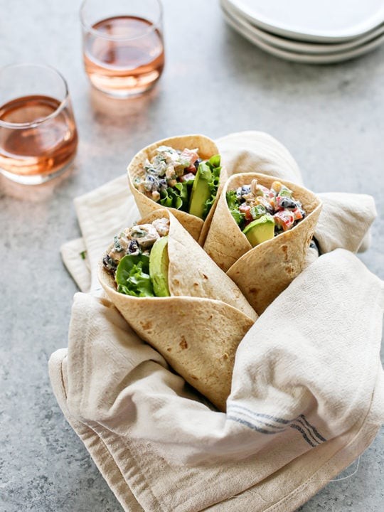 A beautifully assembled hearty chicken wrap, cut in half, with fresh ingredients visible, on a wooden cutting board with a side salad and dipping sauce.