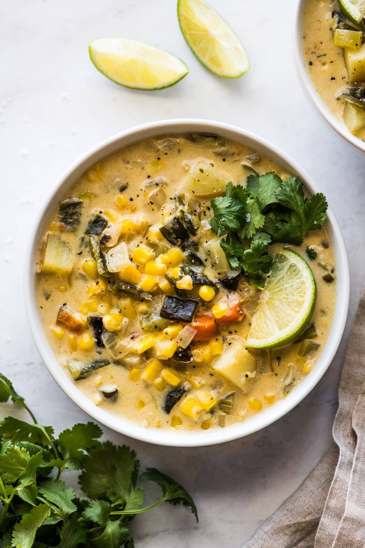 A bowl of roasted corn and poblano soup garnished with cilantro and lime