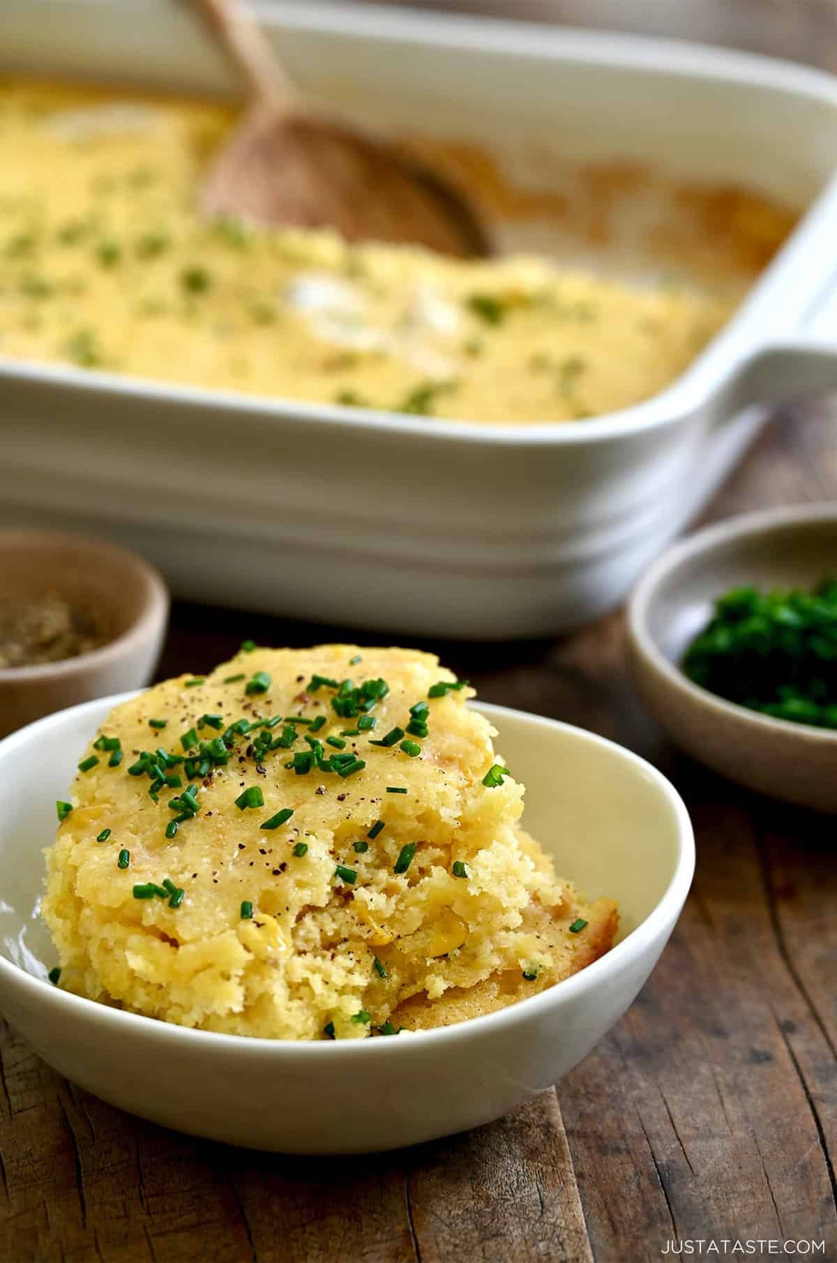 Warm corn casserole with a smooth, creamy texture, garnished with fresh chives, in a rustic baking dish on a wooden table.