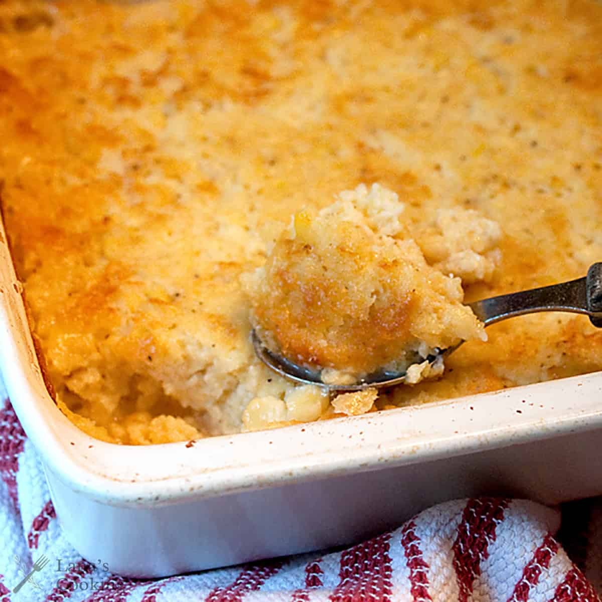 golden brown corn casserole in a rustic baking dish with a spoon scooping a portion, showing crispy edges
