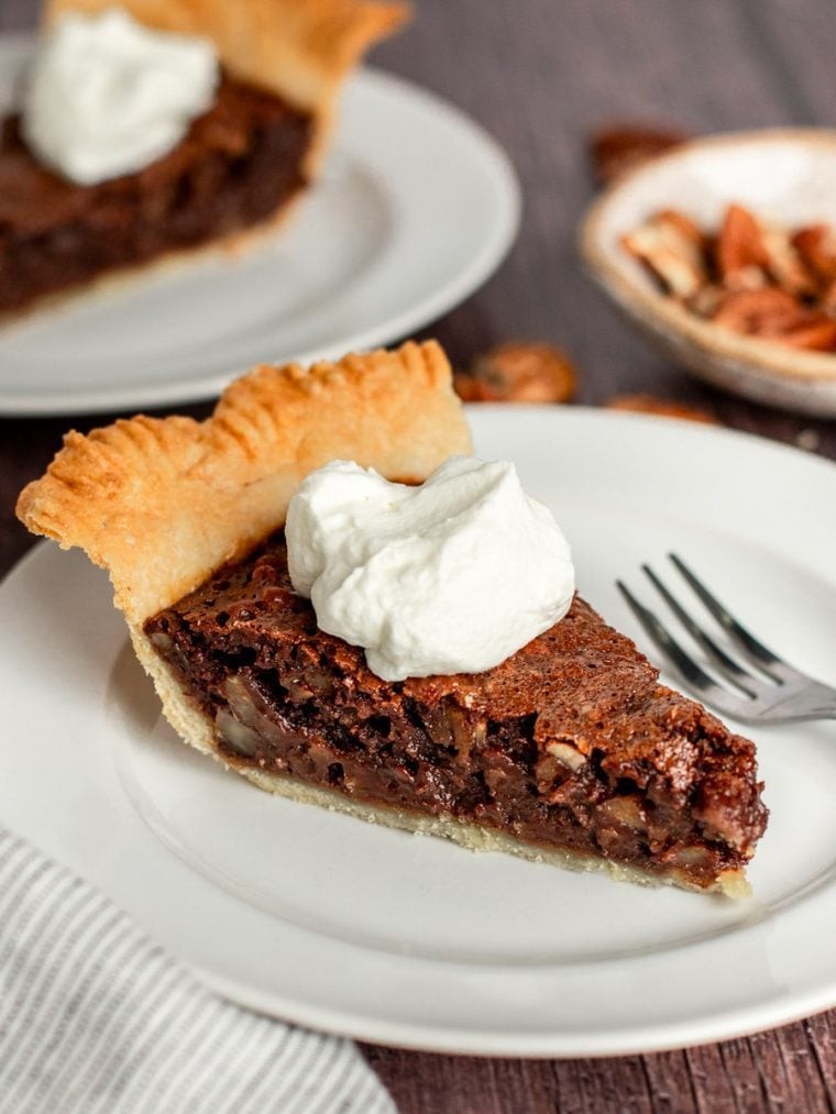 Close-up of a slice of fudgy chocolate pecan pie on a plate, warm, with a scoop of vanilla ice cream