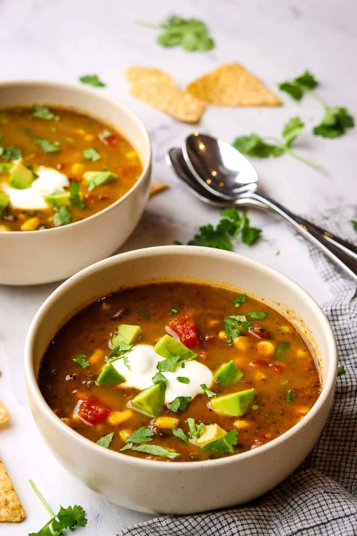 A vibrant bowl of vegan corn and black bean soup topped with avocado and cilantro